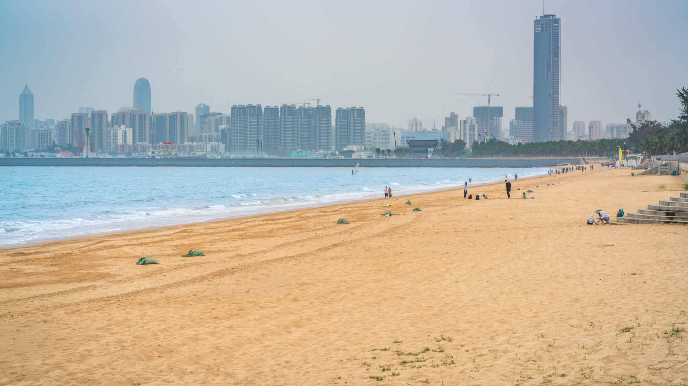  Personnes sur le sable avec la ville d'Haikou en arrière-plan, à Hainan, en Chine.

