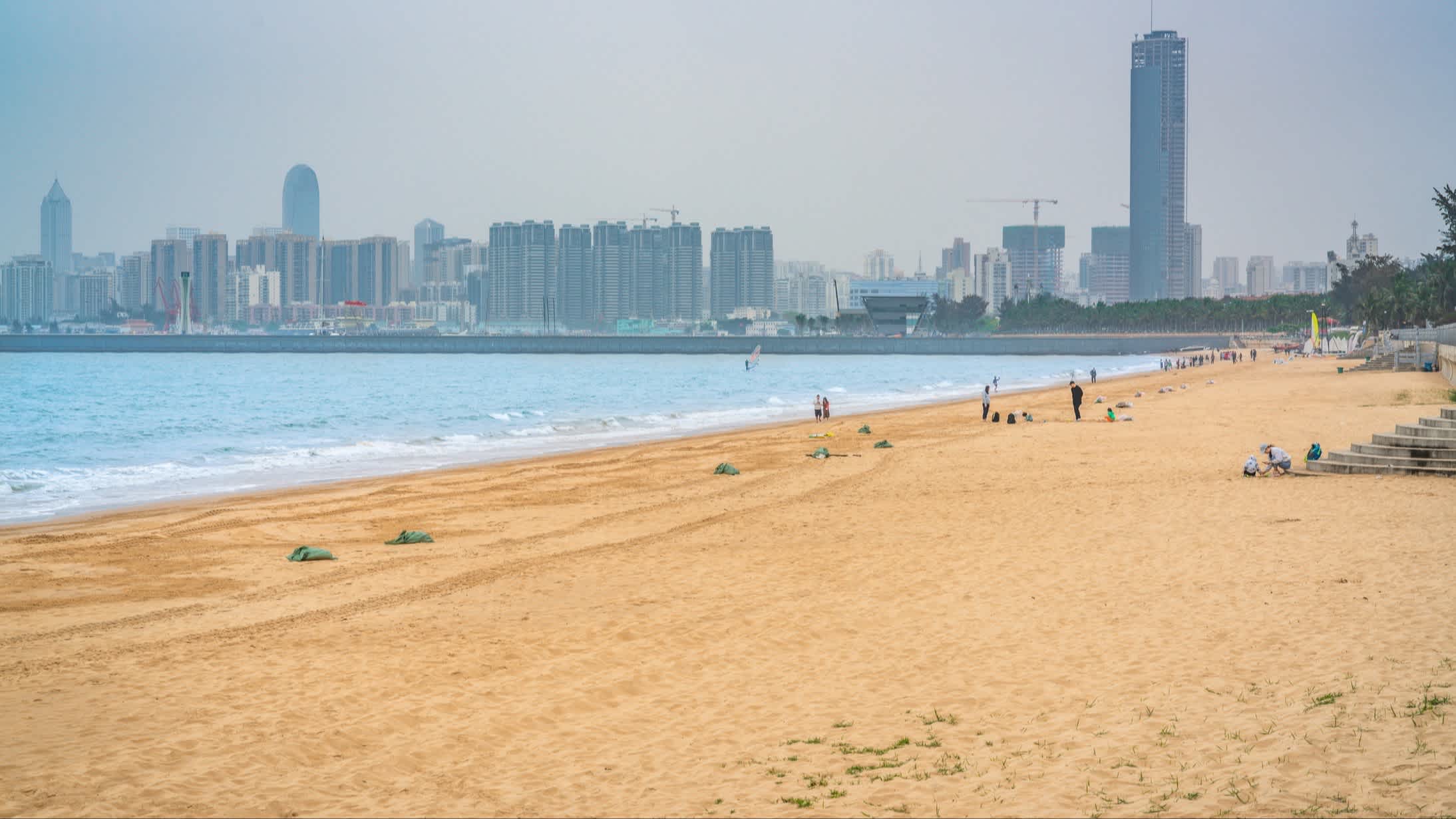 Haikou Xixiu (Holiday Beach) Strandblick in Haikou, Hainan, China mit goldenem Sand und Hochhäusern im Bild.

