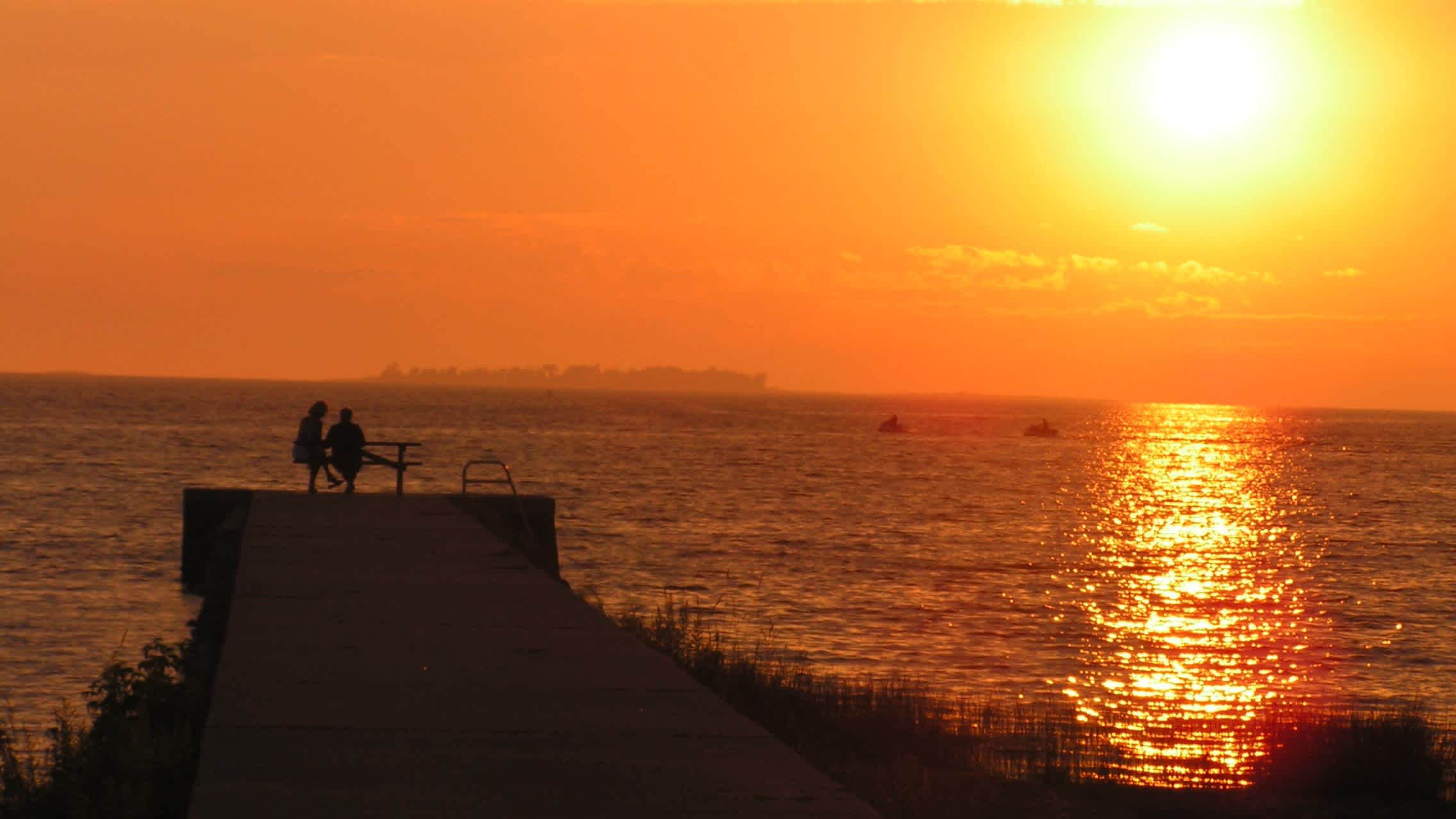 Blick auf einen Steg mit zwei Menschen darauf am Strand Sauble Beach in Ontario, Kanada bei herrlichem Sonnenuntergang.