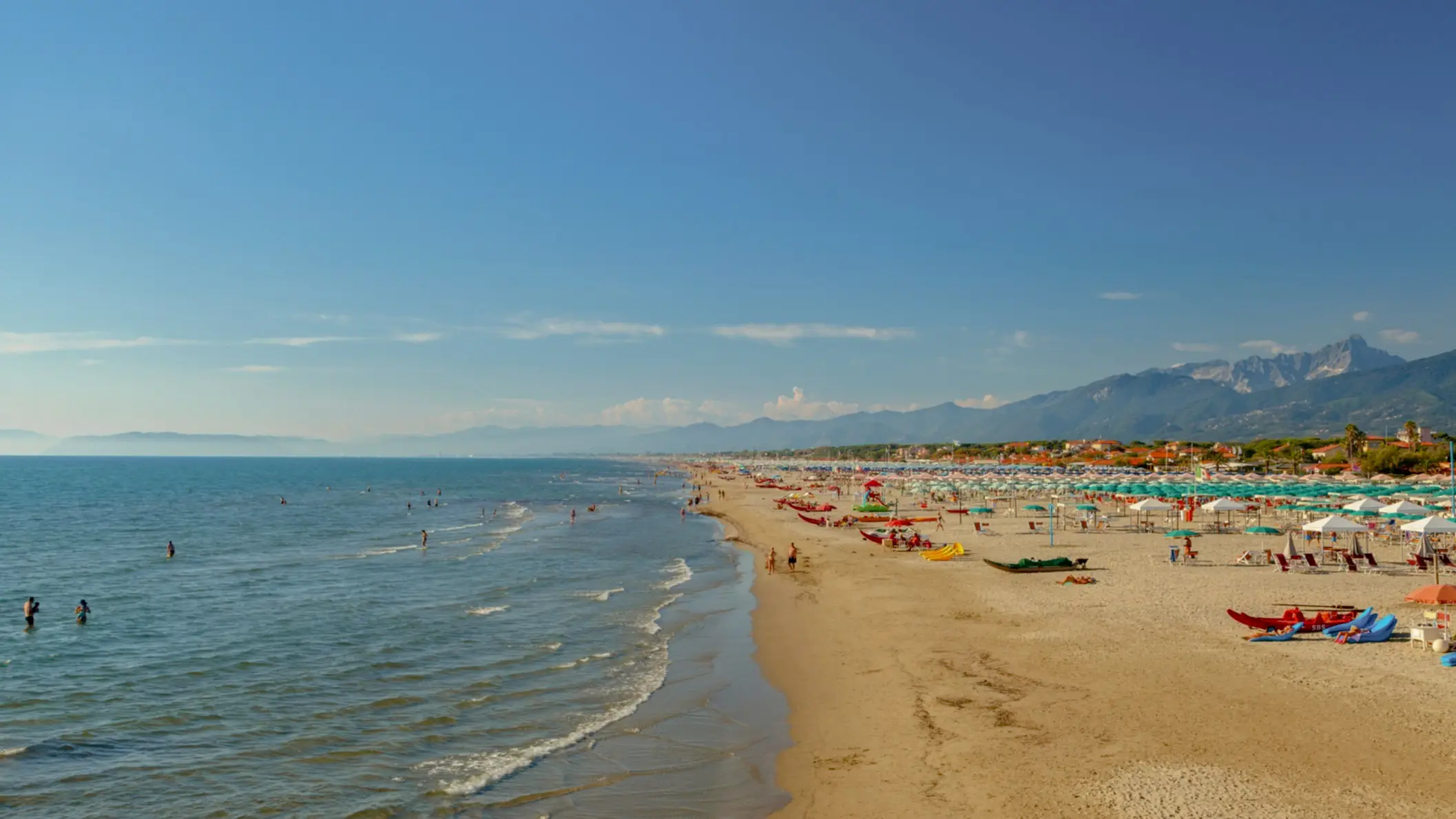 Italien, Toskana, Marina di Pietrasanta Blick auf den goldenen Sandstrand von Marina di Pietrasanta, Toskana, Italien mit vielen Menschen am Strand, Sonnenschirmen und den Bergen im Hintergrund.