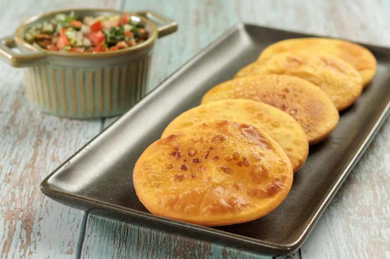 Chile, Sopaipillas Sopaipillas von Kürbis oder Kürbis auf einem rechteckigen Teller auf einem Holztisch und einer Schüssel mit Pebre. Typisches chilenisches Essenskonzept.