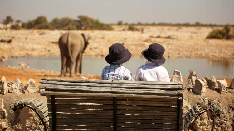 Kinder beobachten Elefanten im Wasserloch Okaukuejo im Etosha Nationalpark, Namibia. 