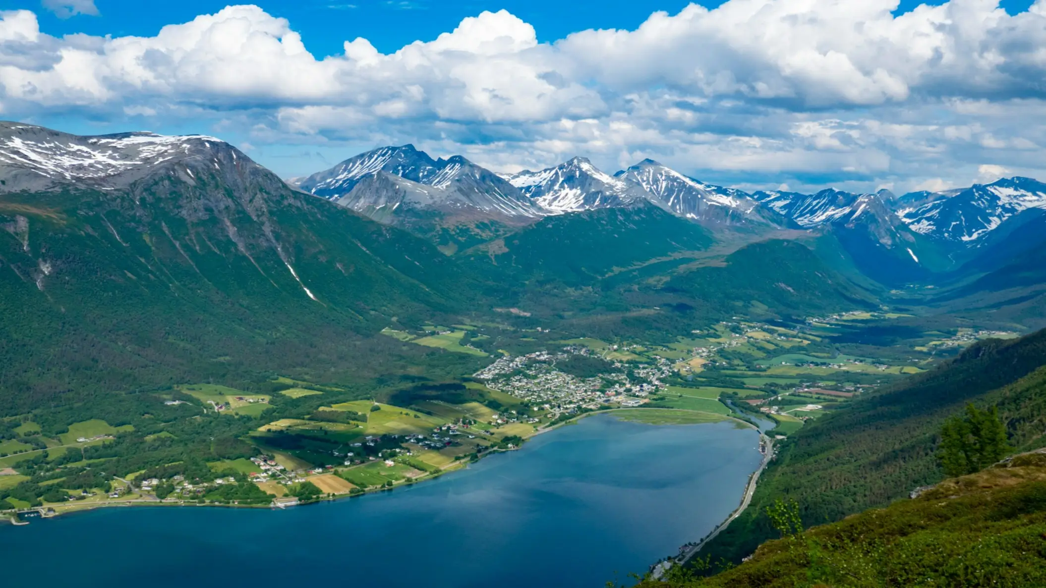 Une vallée avec un lac entouré de montagnes enneigées et de paysages verdoyants, Romsdalsfjord, Norvège.

