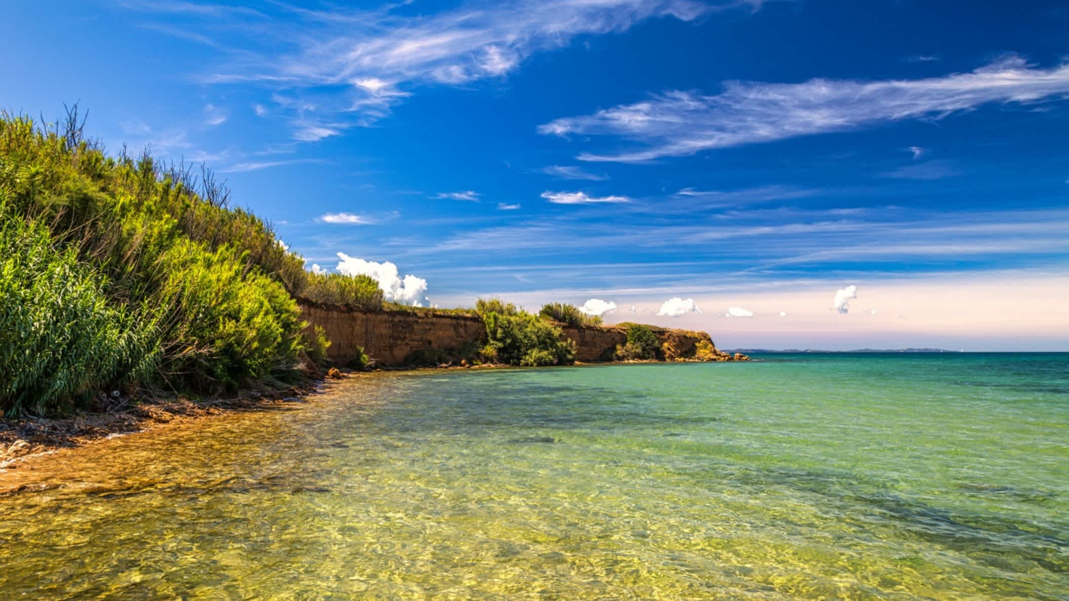 Der Strand auf Privlaka, Kroatien mit Blick auf das Wasser und eine Mauer am Strand mit natürlicher Vegetation.