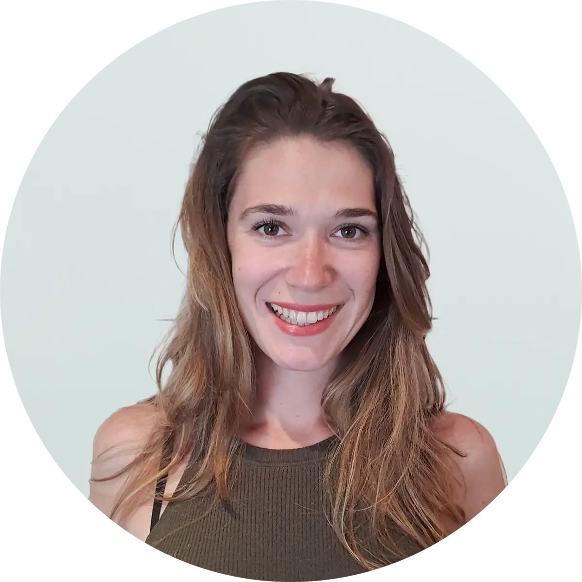 Porträtfoto einer lächelnden Person mit braunen, schulterlangen Haaren in einem olivgrünen Oberteil vor hellgrauem Hintergrund.