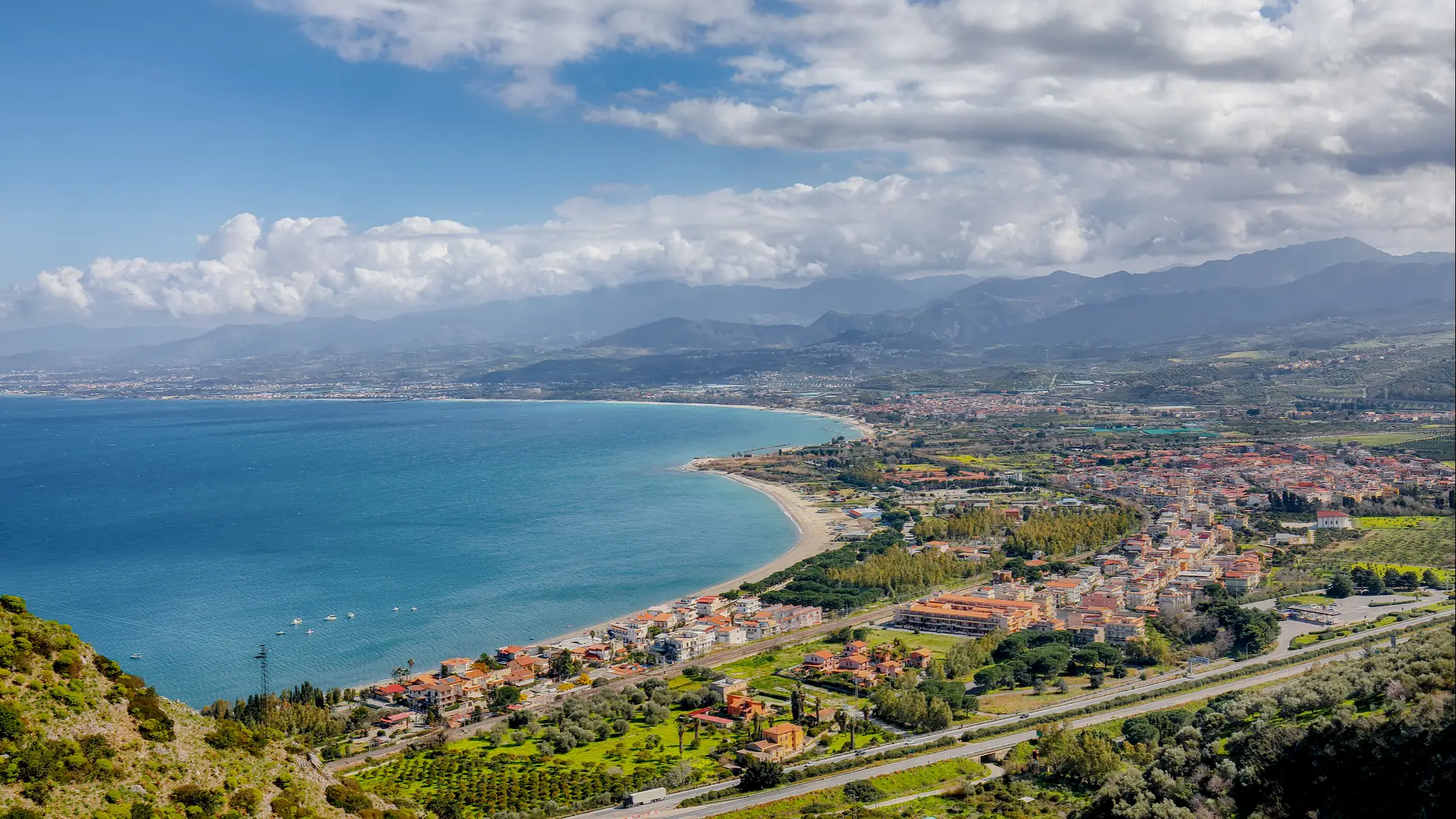 Blick aus der Luft auf eine Stadt und einen Strand in Oliveri  Sizilien, Italien mit Gebirge im Hintergrund.

