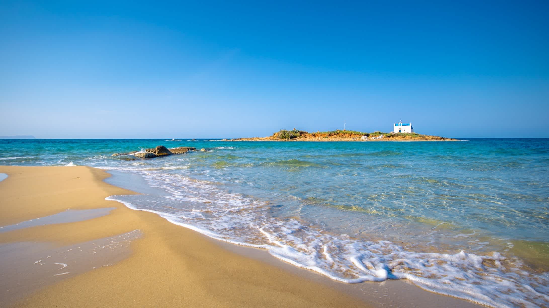 Sandstrand mit einer alten weißen Kirche auf einer einsamen Insel, Malia, Kreta, Griechenland.