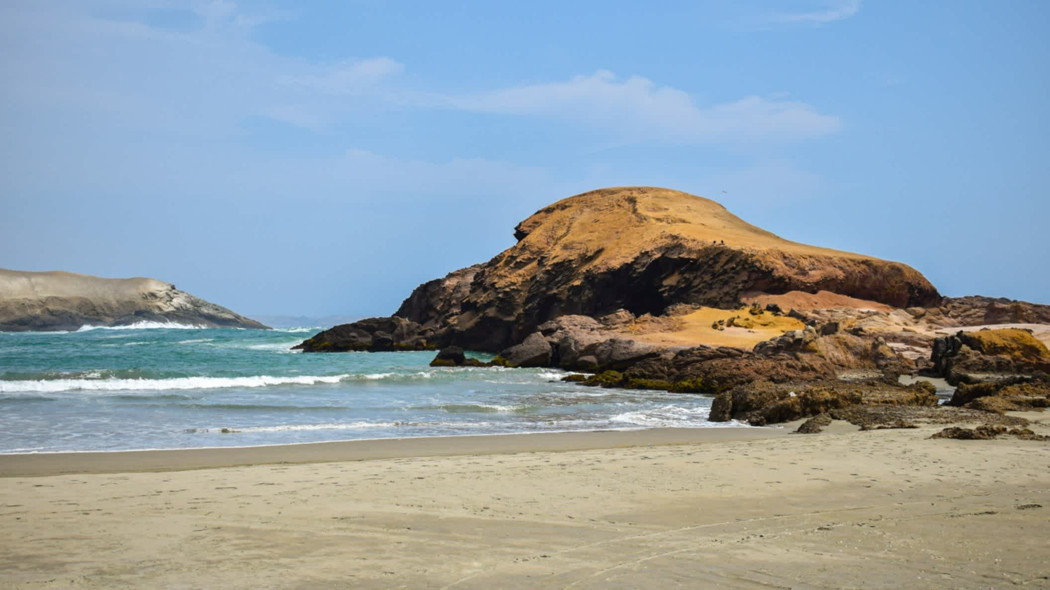 Der Strand Peru Caleta in San José, Peru mit Felsen im Bild, dem blauen Himmel sowie Meer.