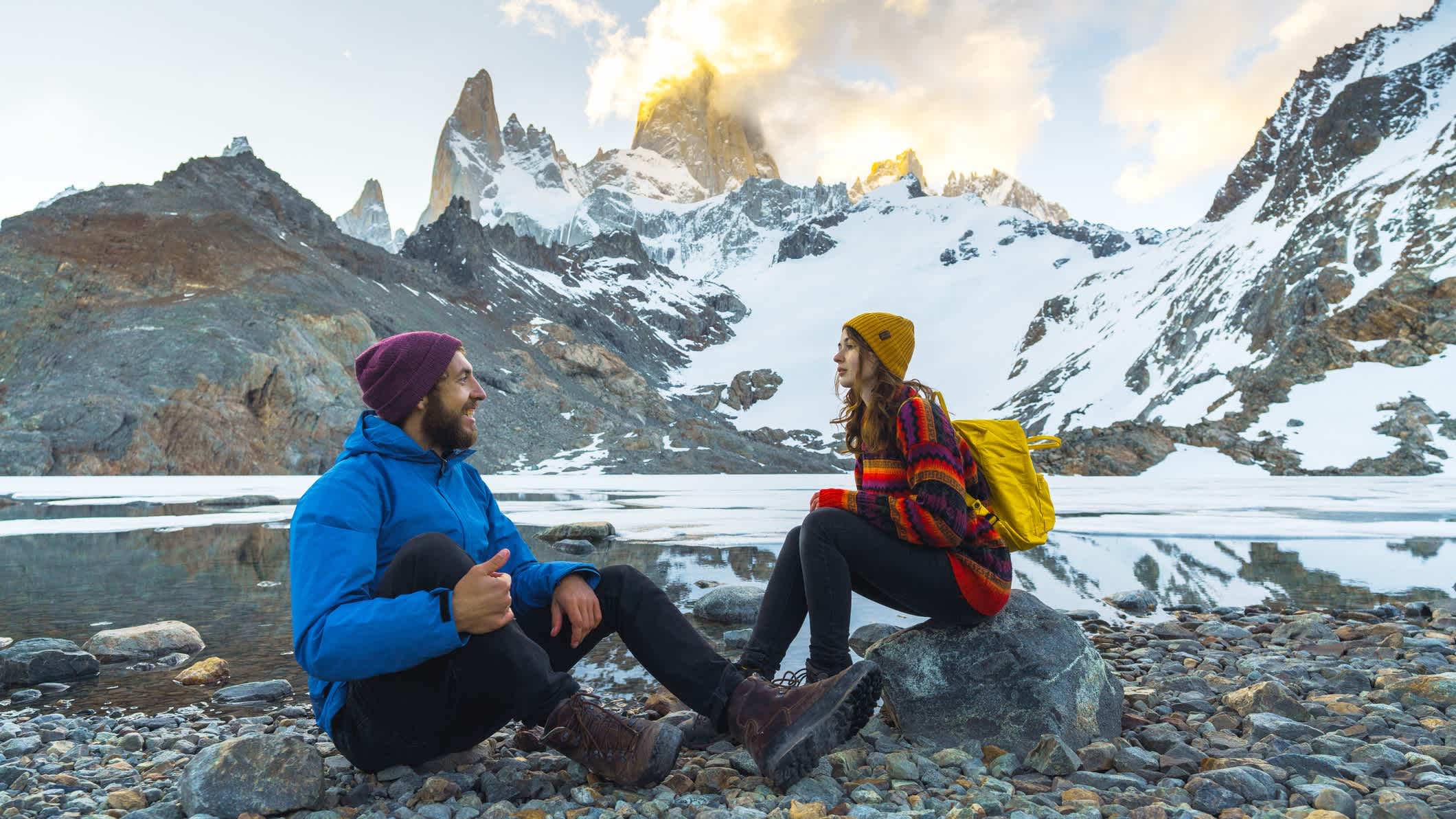 Un homme et une femme assis au bord d'un lac avec le mont Fitz Roy en Patagonie, Chili.