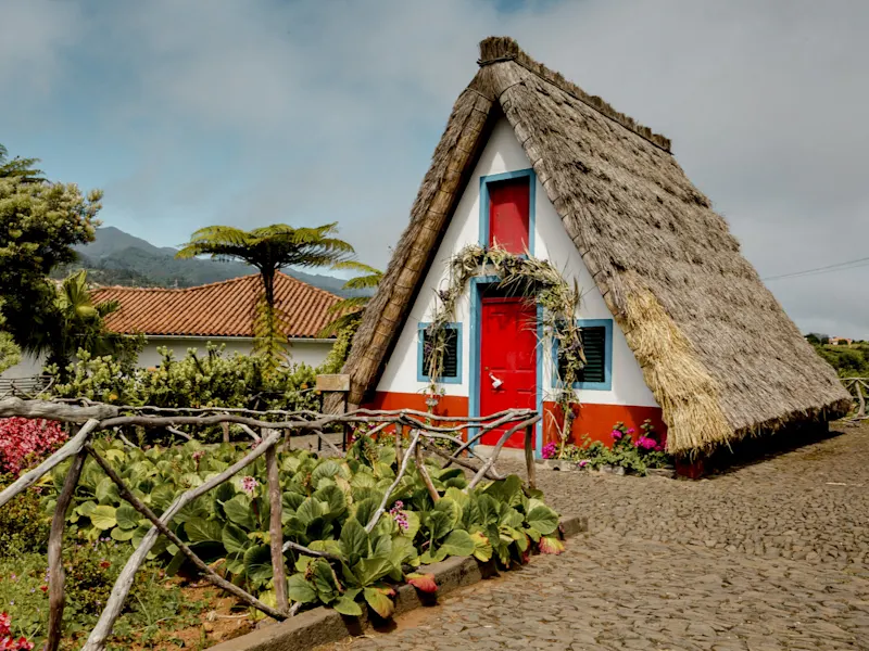 Traditionelles Strohdachhaus mit roter Tür und Garten. Santana, Madeira, Portugal.
