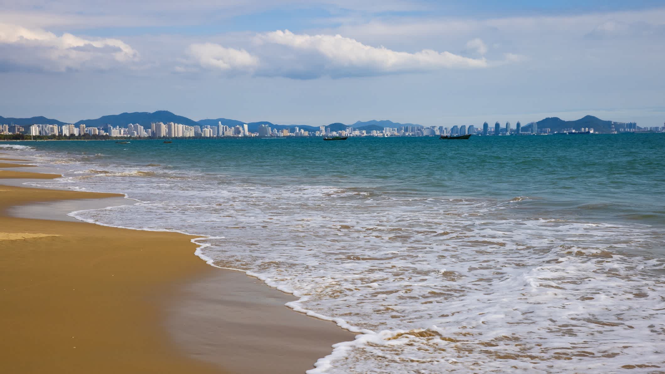 Vue de la mer sur le sable avec la ville de Sanya en arrière-plan à Hainan, en Chine

