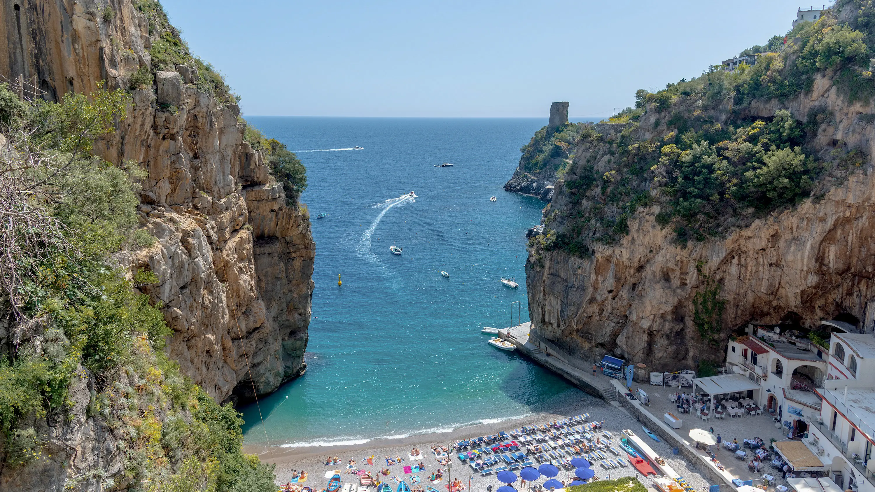 Aerial view of the Marina di Praia bay between steep cliffs and green vegetation