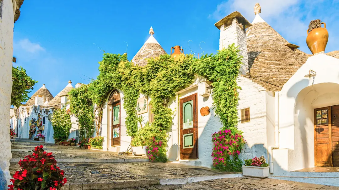 Trulli-Häuser mit Blumen und Efeu unter blauem Himmel. Alberobello, Apulien, Italien