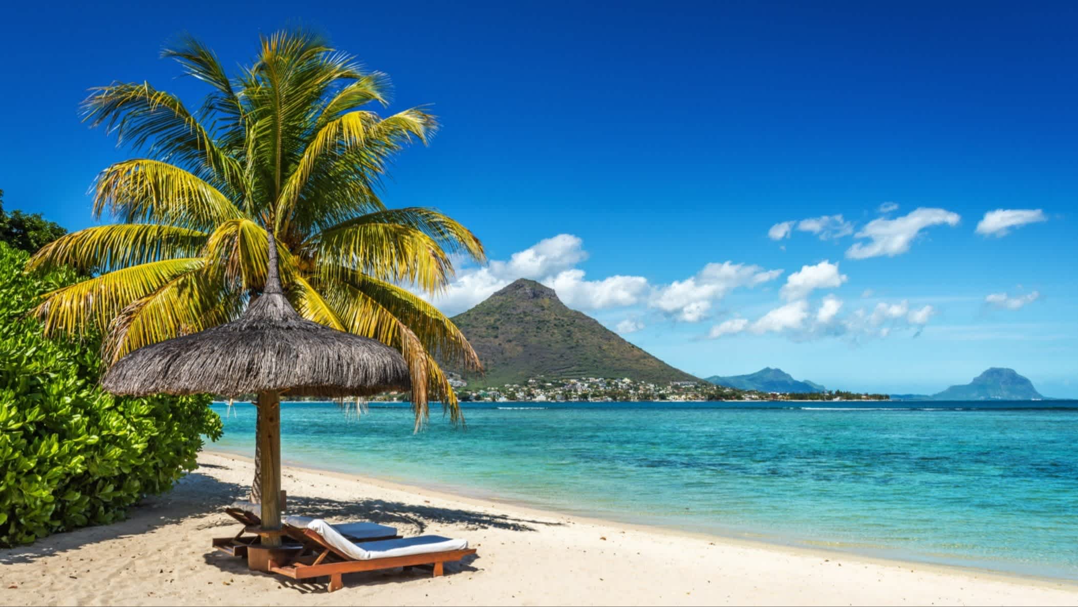 Liegen und Sonnenschirm am Strand von Blue Bay Beach, Südosten, Mauritius mit Palmen im Bild und bei herrlichem Sonnenschein.