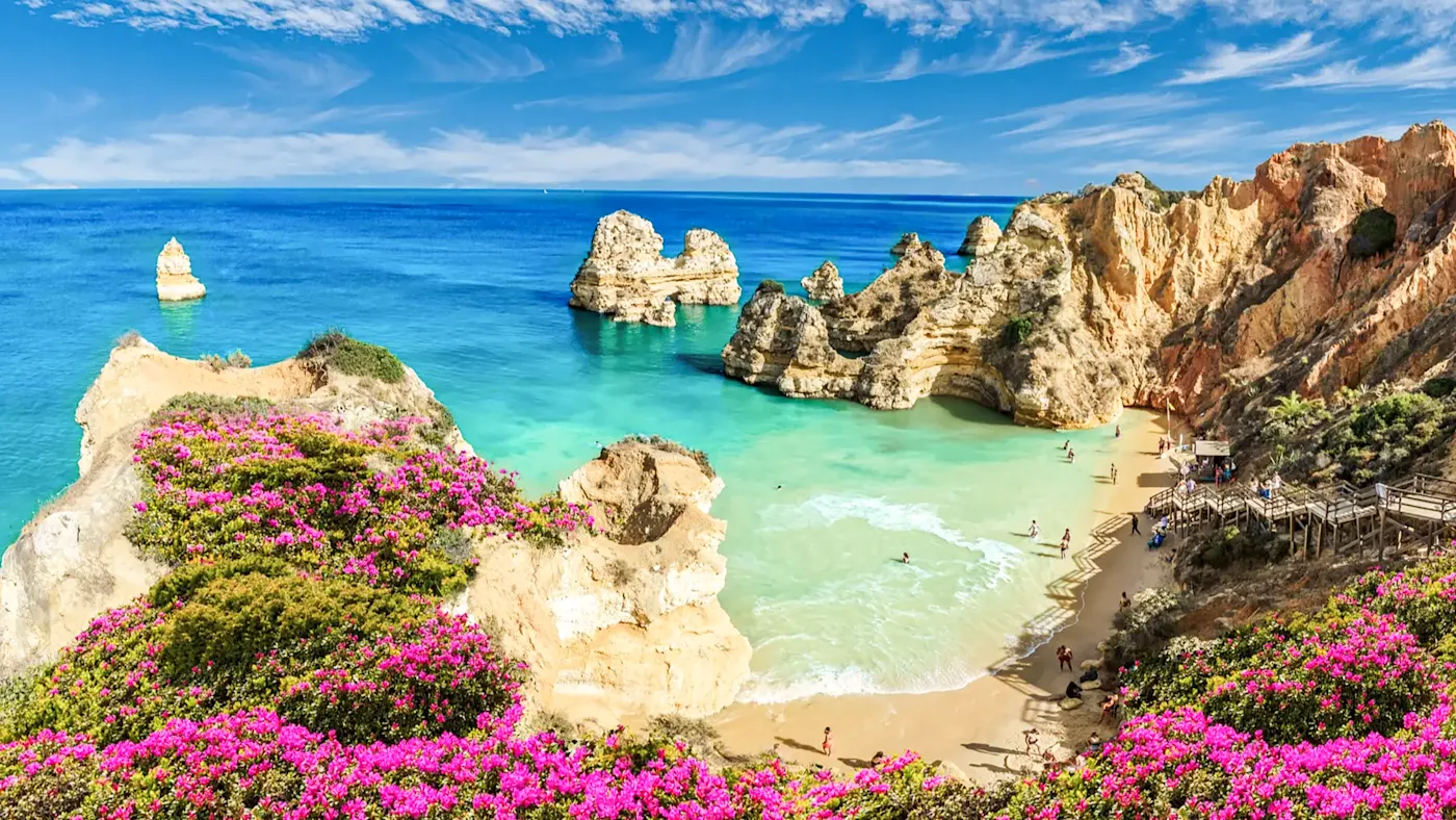 Portugal, Algarve, Lagos Sandstrand mit Felsen und pinken Blumen. Lagos, Algarve, Portugal.