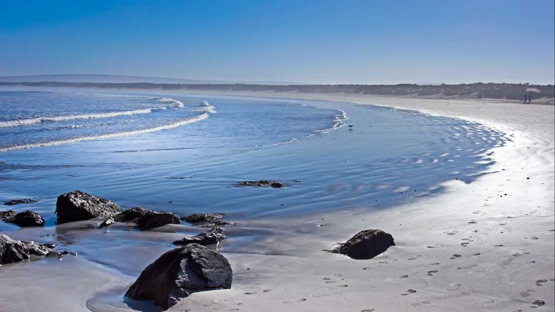 Breiter Strand mit kleinen Wellen am frühen Morgen in Paternoster, Südafrika
