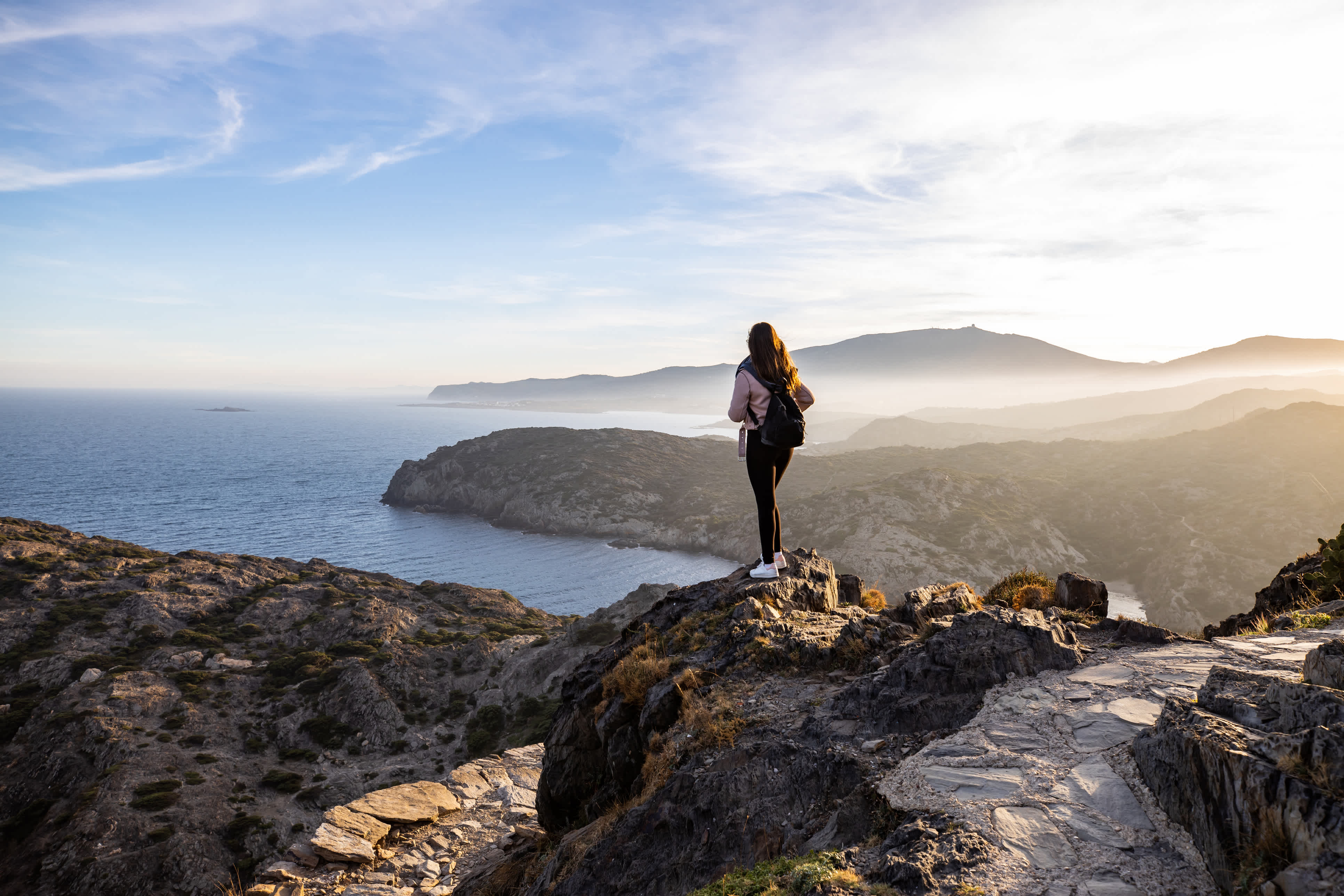 Schöne Frau steht auf einer Klippe bei Sonnenuntergang mit dem Mittelmeer im Hintergrund am Cap de Creus, in Spanien mit Kopierraum