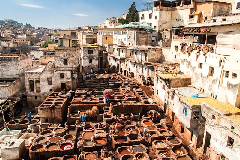 Traditionelle Gerberei in Fes, Marokko mit zahlreichen Färbebecken zwischen alten Gebäuden unter blauem Himmel.