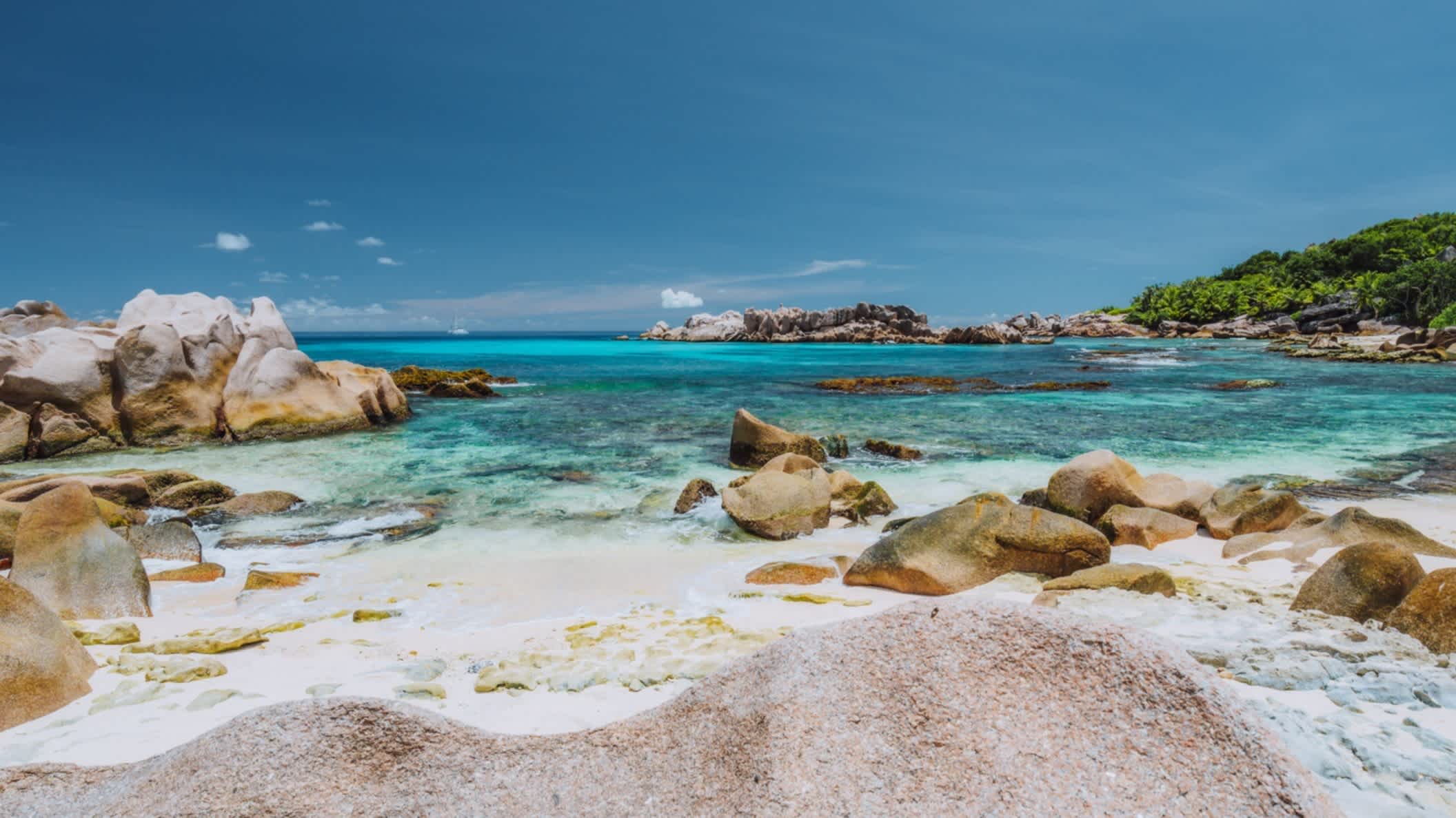 Sonniges Wetter am Anse Cocos Strand auf der Insel La Digue Island, Seychellen mit blauem Meer und typischen Granitfelsen im Bild.