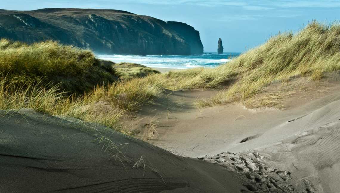 Vue de la baie de Sandwood en Écosse depuis les chemins de sable avec les falaises et la mer en arrière plan.