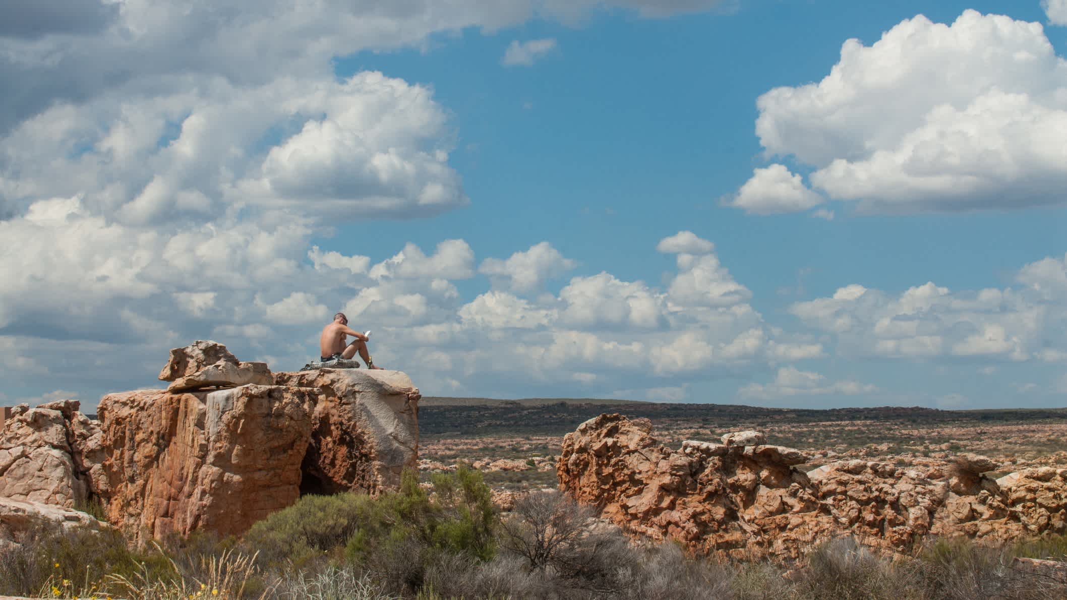 Un homme est assis sur une grande pierre et regarde au loin au Kagga Kamma Nature Reserve en Afrique du Sud