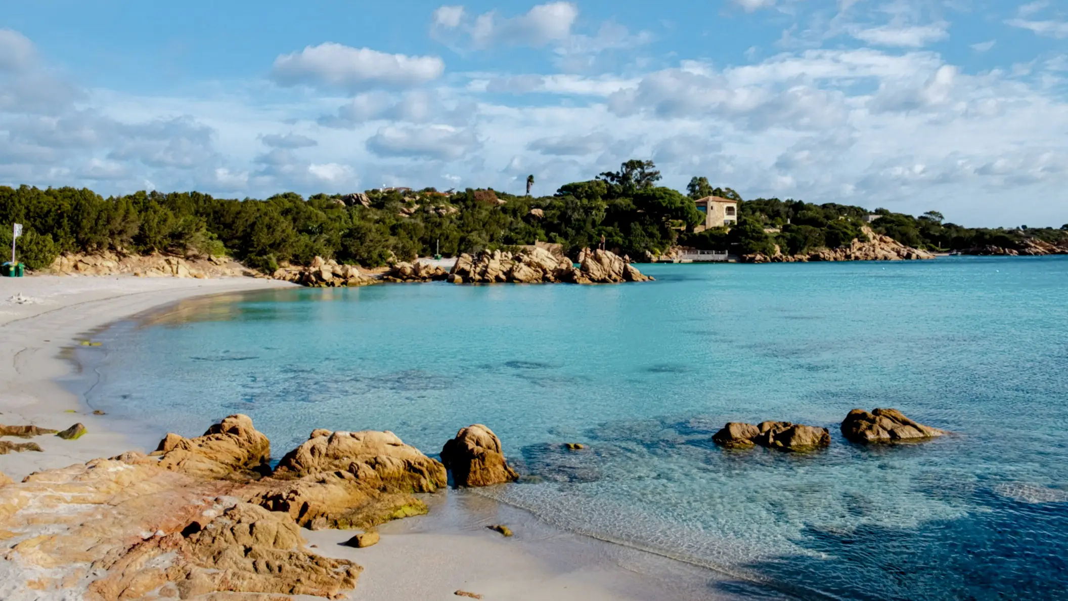 Blick zum Capriccioli-Strand an der Costa Smeralda, Sardinien, Italien mit Steinen im Bild sowie bei schönem Wetter.