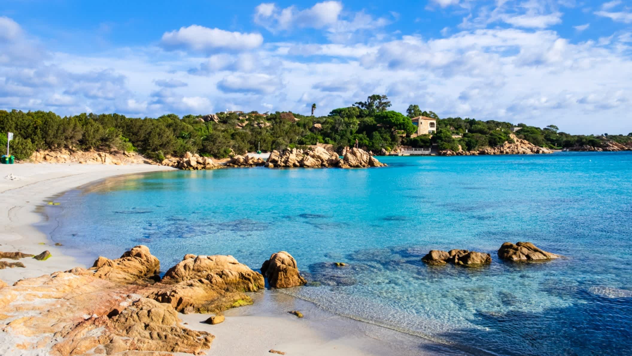 Blick zum Capriccioli-Strand an der Costa Smeralda, Sardinien, Italien mit Steinen im Bild sowie bei schönem Wetter.
