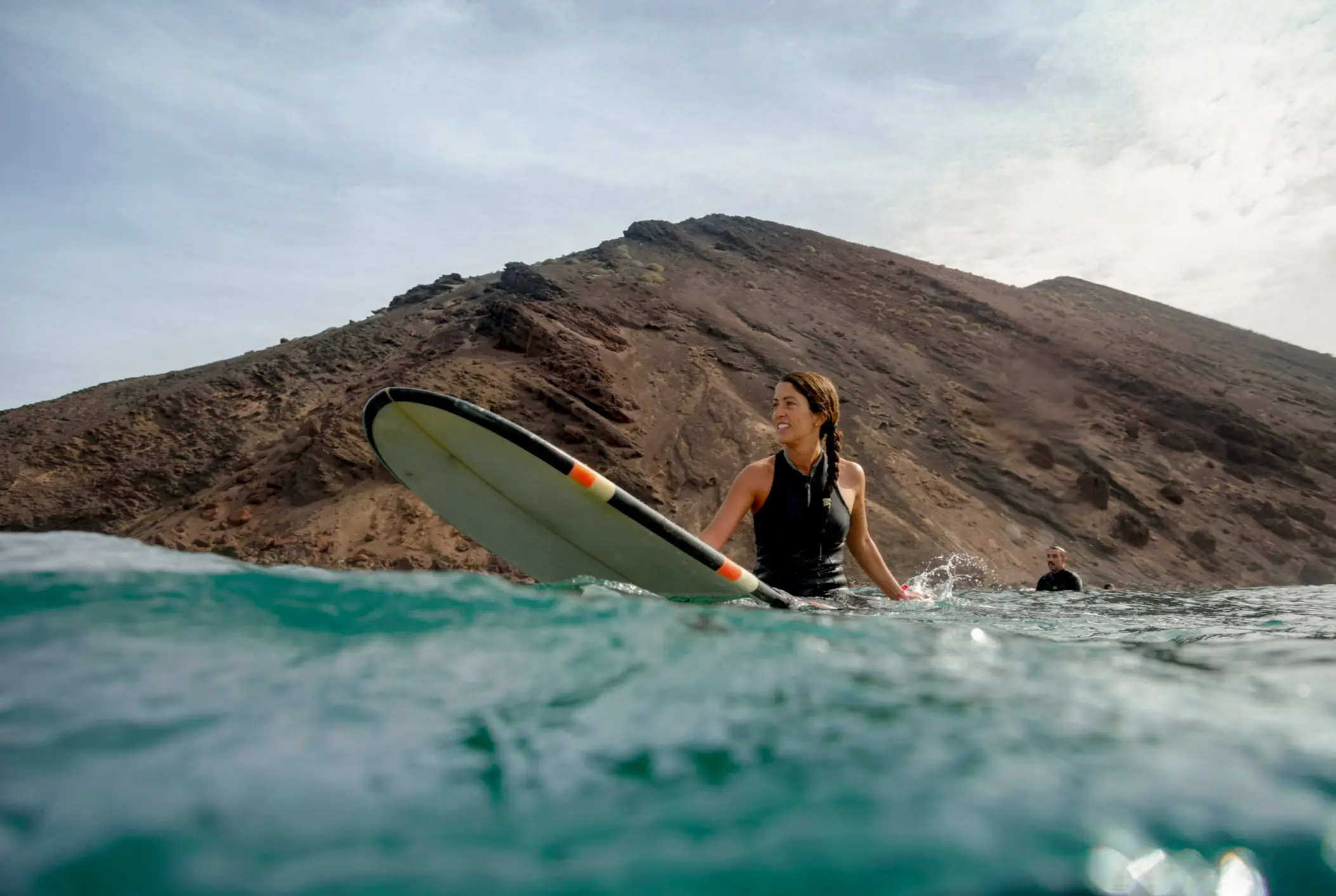 Frau beim Surfen auf Fuerteventura im Atlantischen Ozean vor dem Hintergrund von blauem Himmel, Wolken und transparenten Wellen