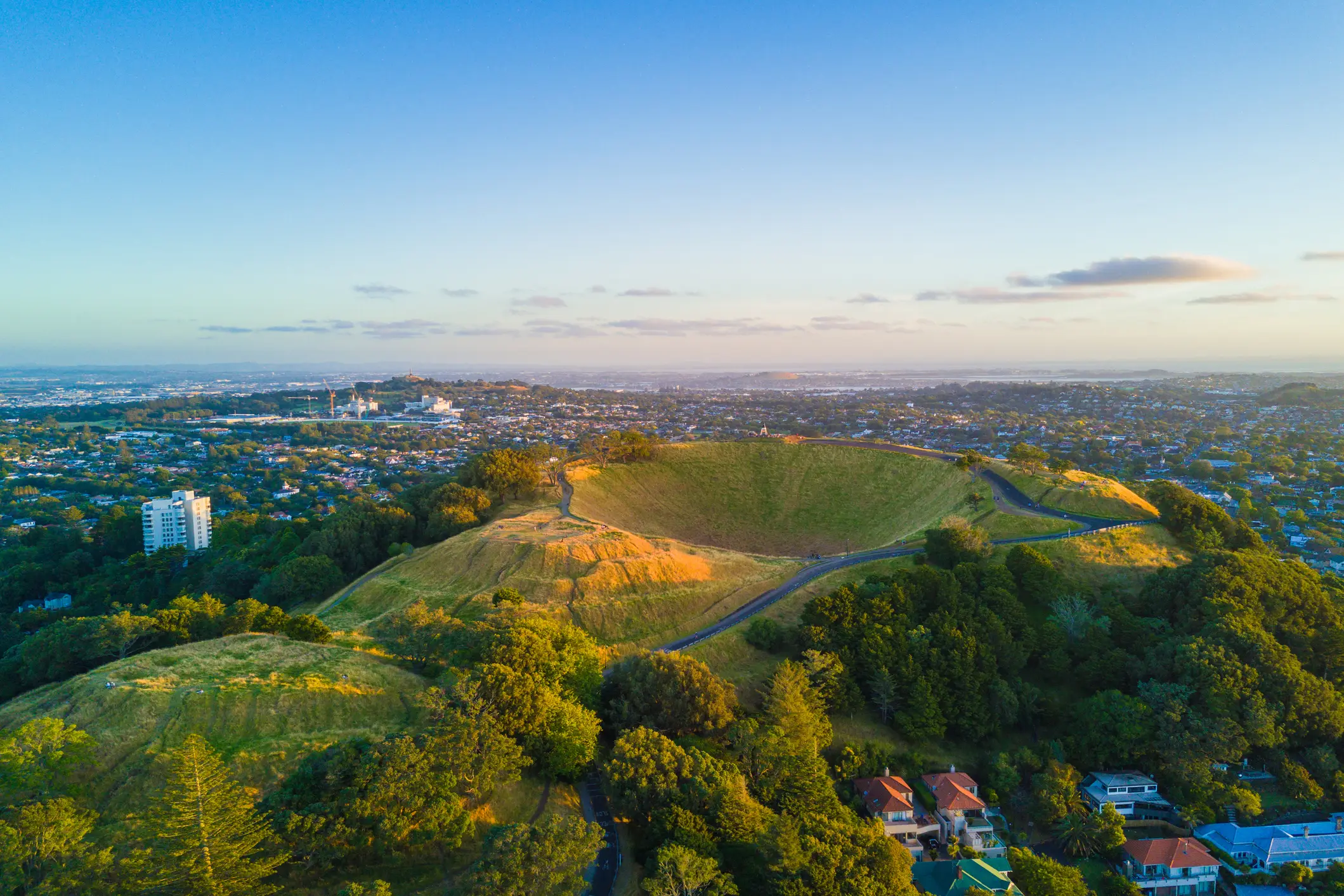 Collines verdoyantes du Mont Eden avec cratère et quartiers environnants au coucher du soleil, Auckland, Île du Nord, Nouvelle-Zélande.