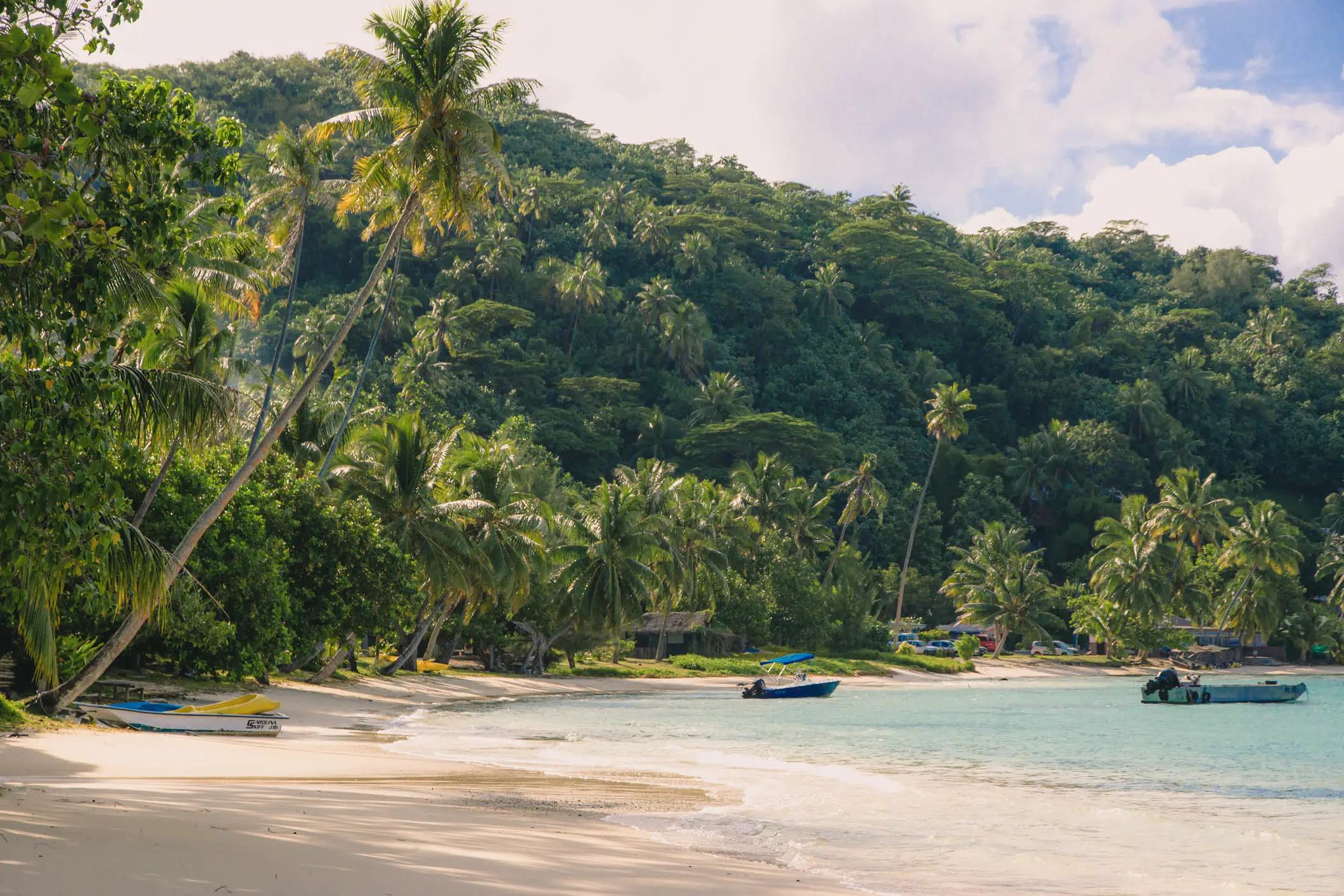 Plage tropicale de Matira avec sable blanc, eau turquoise, palmiers et petits bateaux près du rivage, Bora Bora, Polynésie Française.