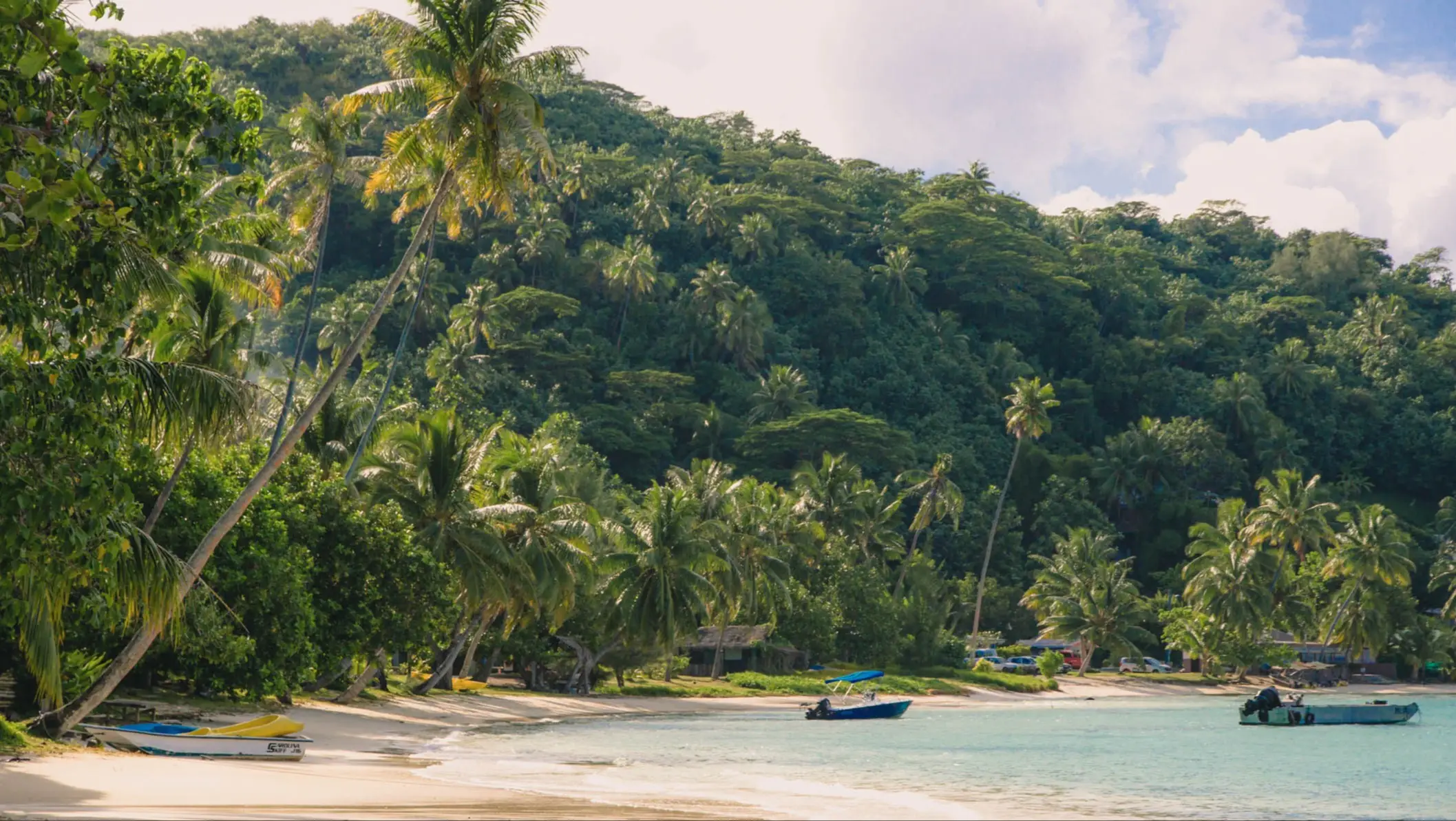 Plage tropicale de Matira avec sable blanc, eau turquoise, palmiers et petits bateaux près du rivage, Bora Bora, Polynésie Française.