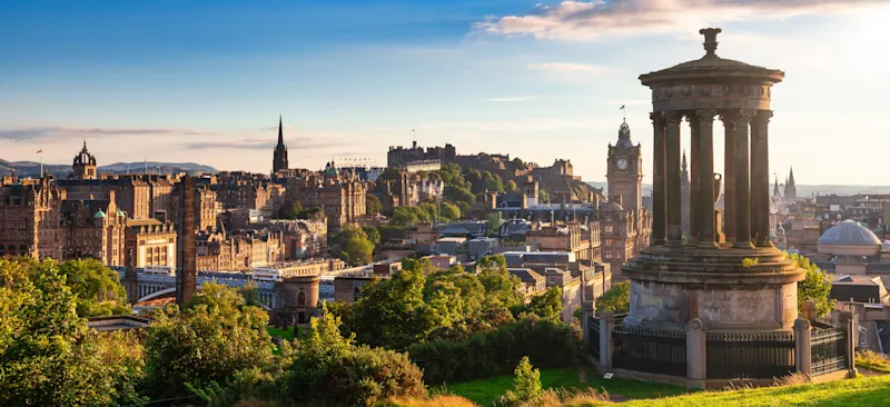 Edinburgh skyline with historic castle, clock tower, and Dugald Stewart Monument in golden evening light.