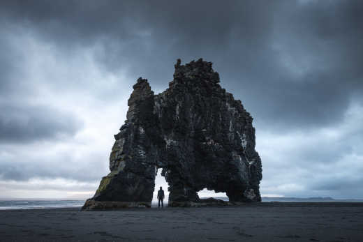 Un homme se tient sous le célèbre rocher Hvitserkur sur une plage noire en Islande.