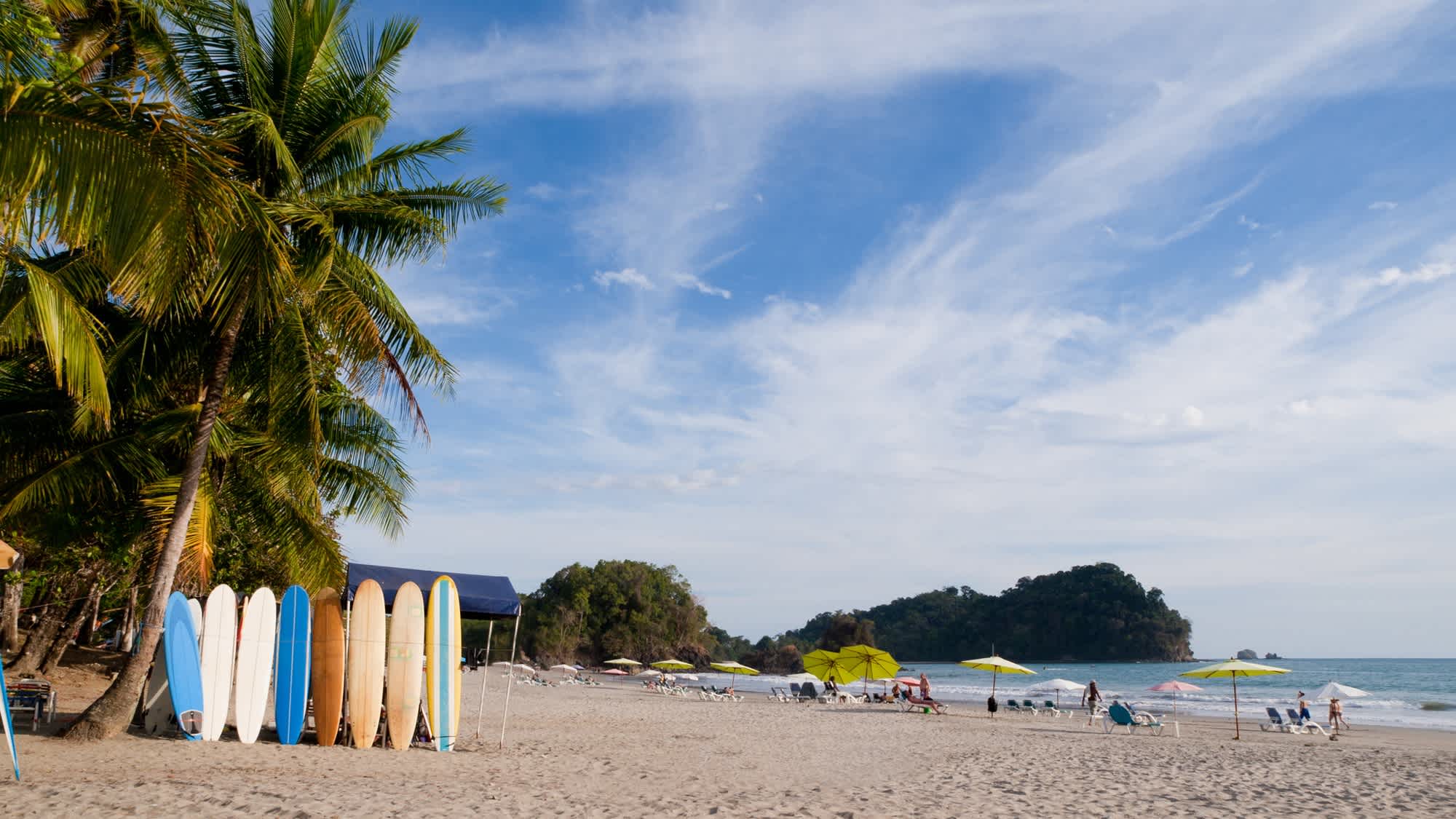 Der Strand von Manuel Antonio in Costa Rica mit Surfbrettern, Palmen und Menschen am Strand bei sonnigem Wetter. 

