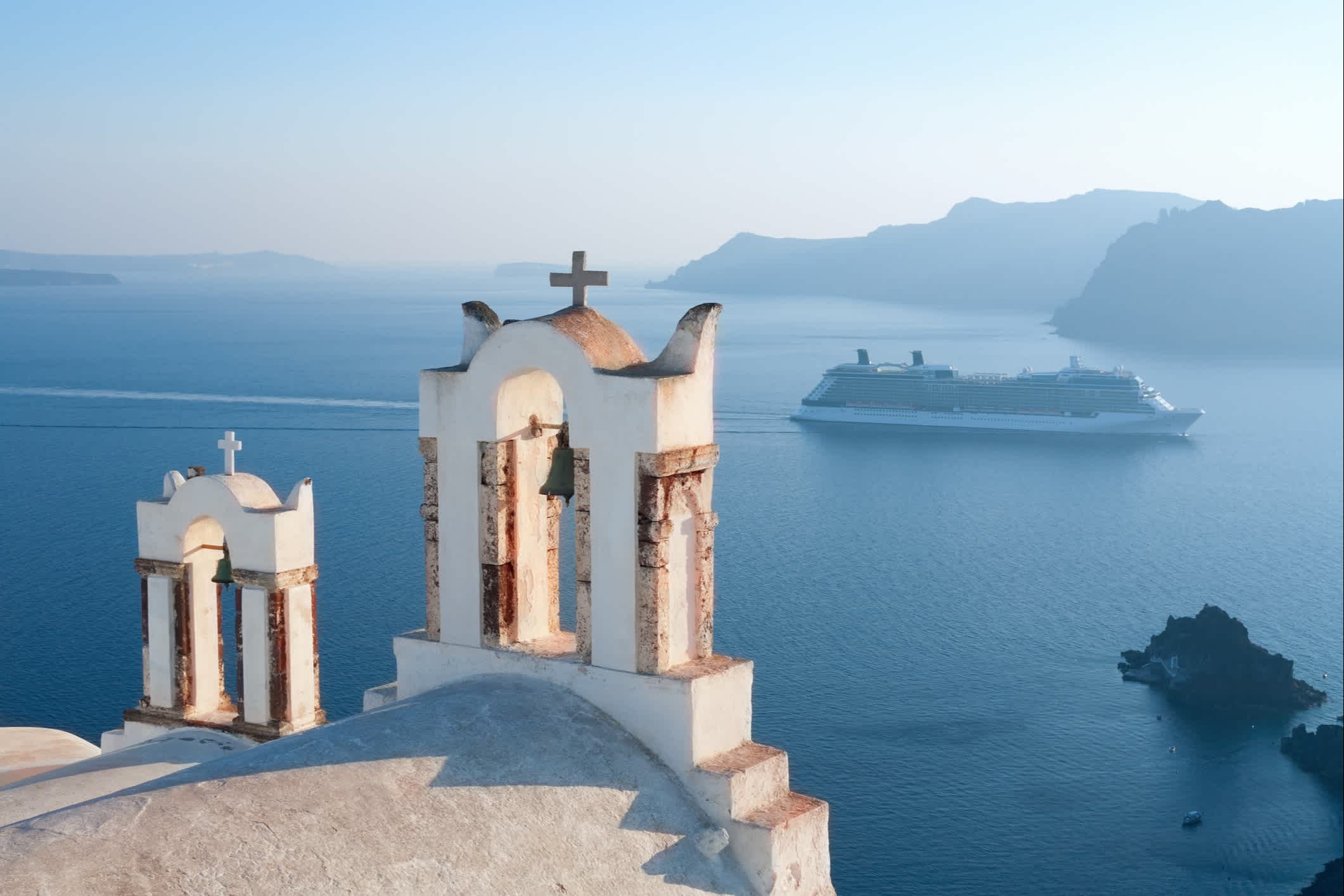 Schöne Aussicht auf die berühmten griechischen Kirchen auf der Mittelmeerinsel Santorin mit einem Kreuzfahrtschiff im Hintergrund. 