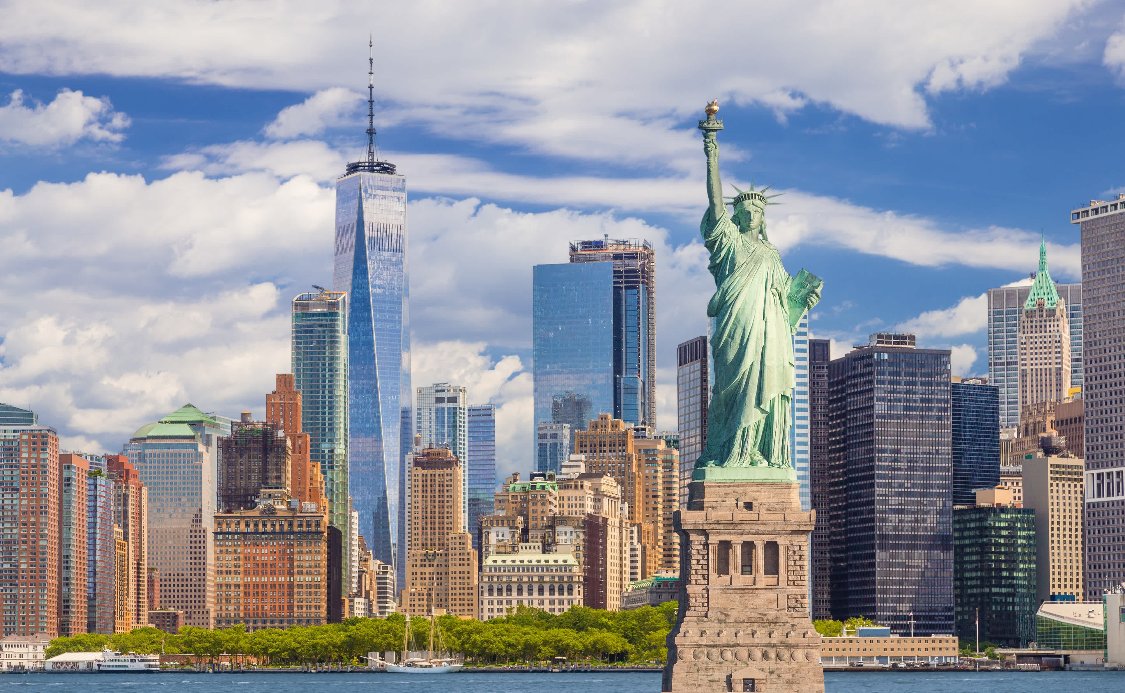 Freiheitsstatue und Skyline von New York mit Manhattan Financial District, World Trade Center, Wasser des Hafen von New York, Battery Park und blauer Himmel.