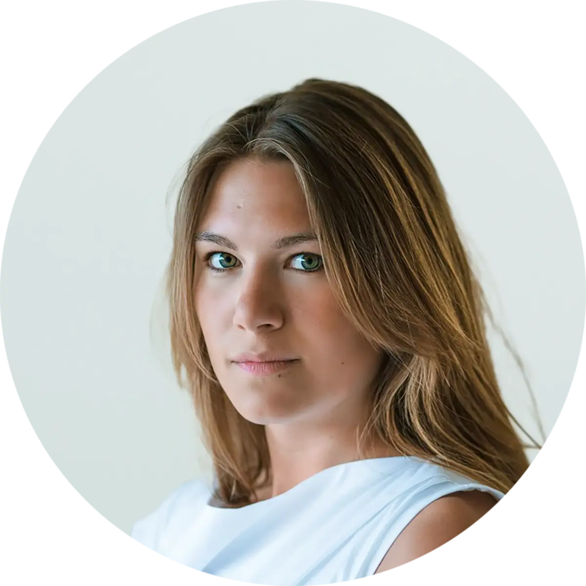 Julia Elfert Porträtfoto einer Person mit braunem Haar und grünen Augen in einem weißen Oberteil vor hellem Hintergrund in runder Rahmung.