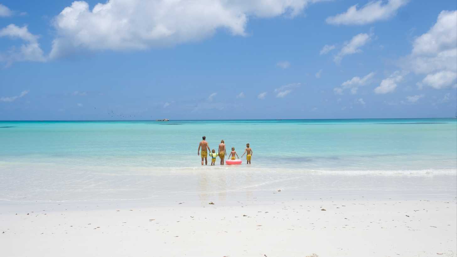 Famille qui se tient la main et se dirige vers l'océan sur une plage de sable blanc et une eau turquoise