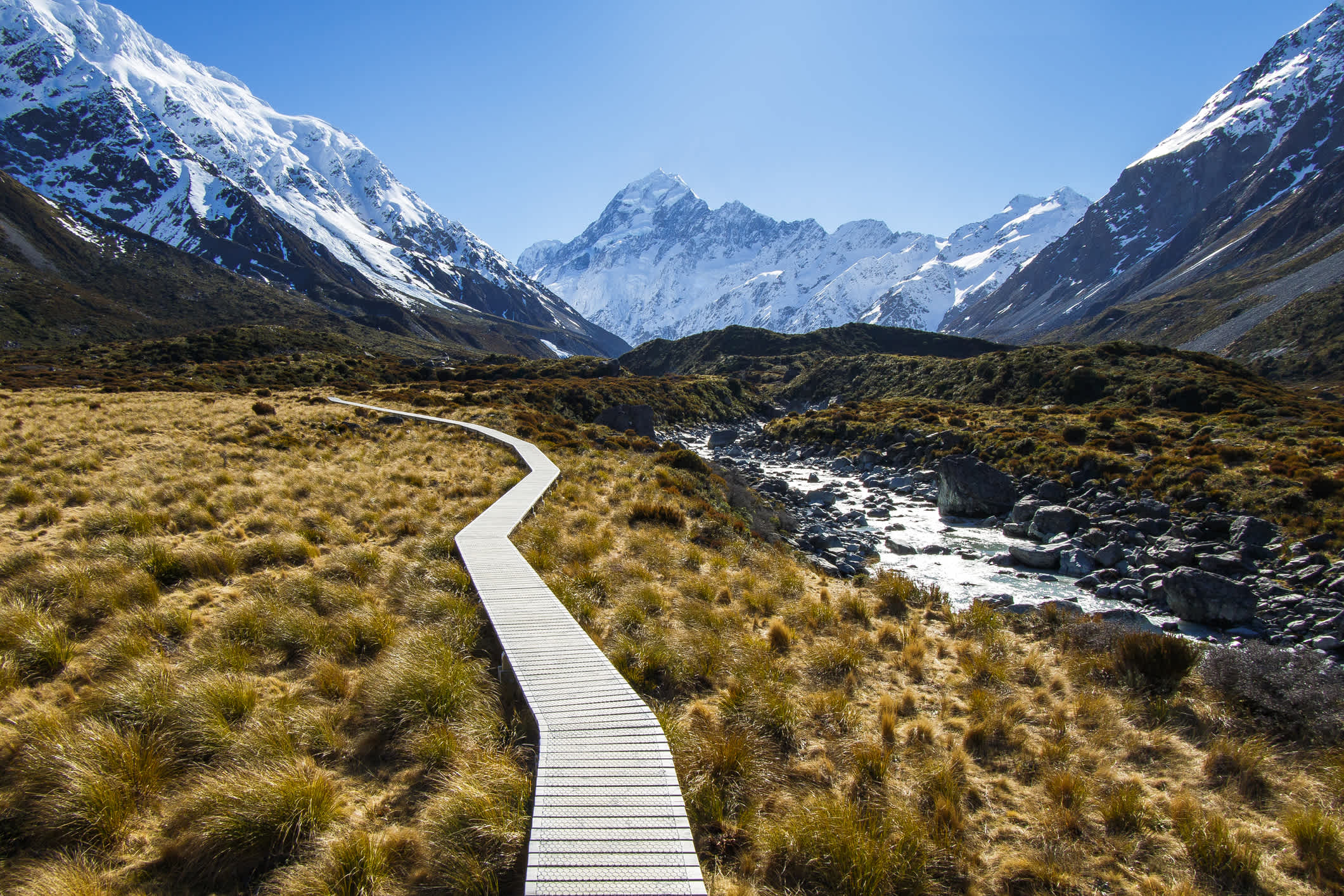 Bergwanderweg in einem Tal, umgeben von schneebedeckten Bergen auf dem Weg zum Mount Cook, Neuseeland