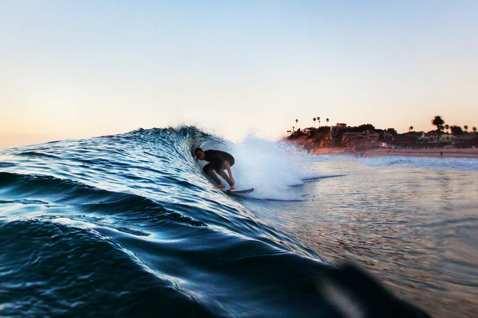 Ein junger Mann surft vor einer Küstenstadt in Kalifornien.
