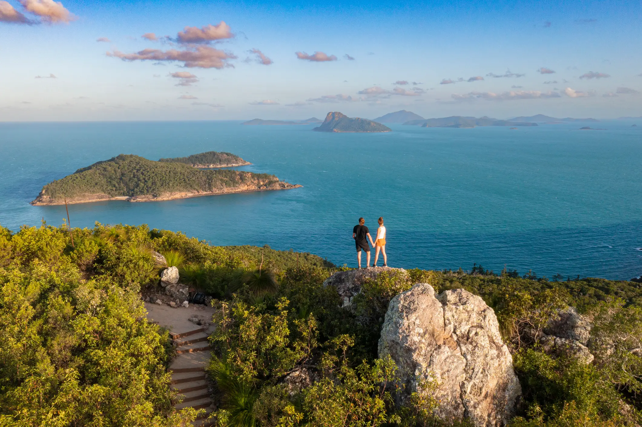 Ein Paar steht auf einem Berg mit Blick auf den tiefblauen Ozean bei Queensland.

