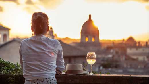Junge Frau mit Glas Weißwein vor Panoramablick auf Rom Stadtbild von Campidoglio Terrasse bei Sonnenuntergang.