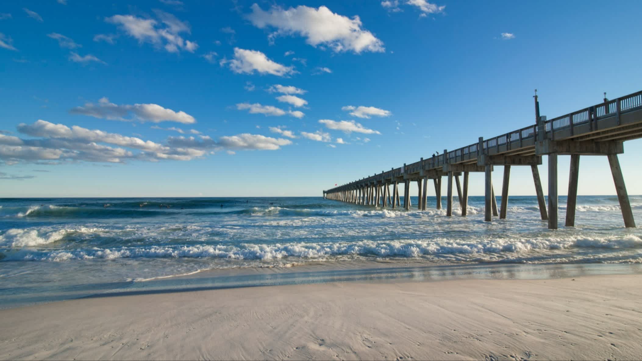 Der Strand Pensacola Beach, Escambia County, Florida, USA bei purem Sonnenschein mit Blick auf einen langen Steg der ins Wasser gebaut ist.