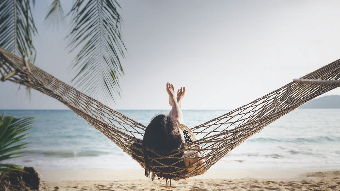 Une femme en train de se relaxer dans un hamac tressé sur une plage tropicale au sable fin.