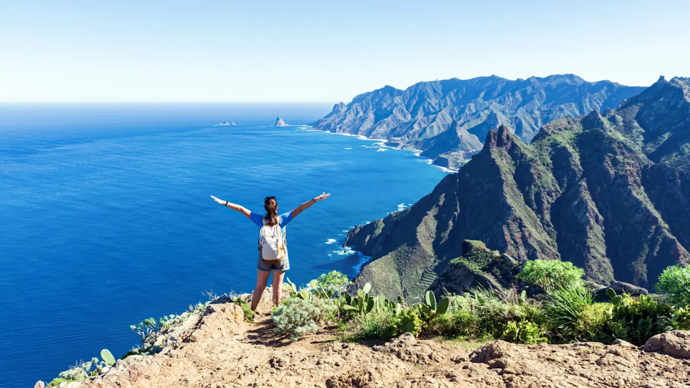 Spanien, Teneriffa, Anaga Frau auf Klippe mit Blick aufs Meer und Berge. Anaga, Teneriffa, Spanien.