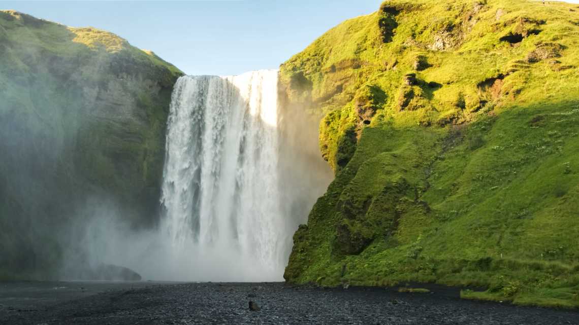 Sonnenlicht fällt über den Skógafoss Wasserfall und die moosbewachsenen Steinwände in Island