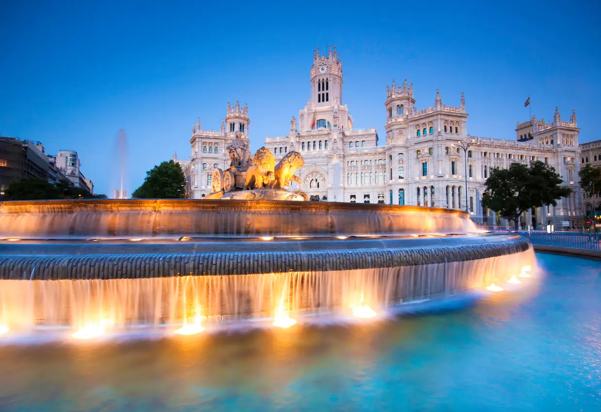 Madrid Der beleuchtete Cibeles-Brunnen mit kaskadenförmigem Wasser vor dem großen Palacio de Cibeles in der Abenddämmerung in Madrid, Spanien, mit einem klaren blauen Himmel im Hintergrund.