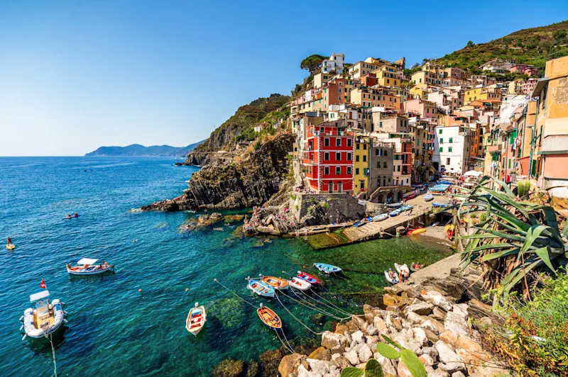 Colorful cliffside village of Cinque Terre, Italy, with vibrant buildings overlooking blue Mediterranean waters and small boats.