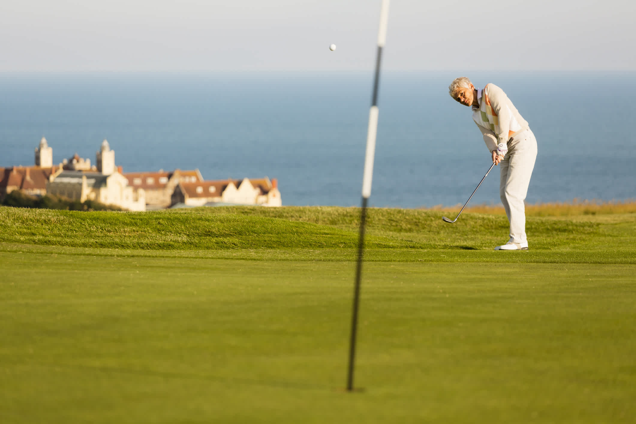 Un golfeur frappe la balle sur le green d'un terrain de golf anglais avec la mer en arrière plan
