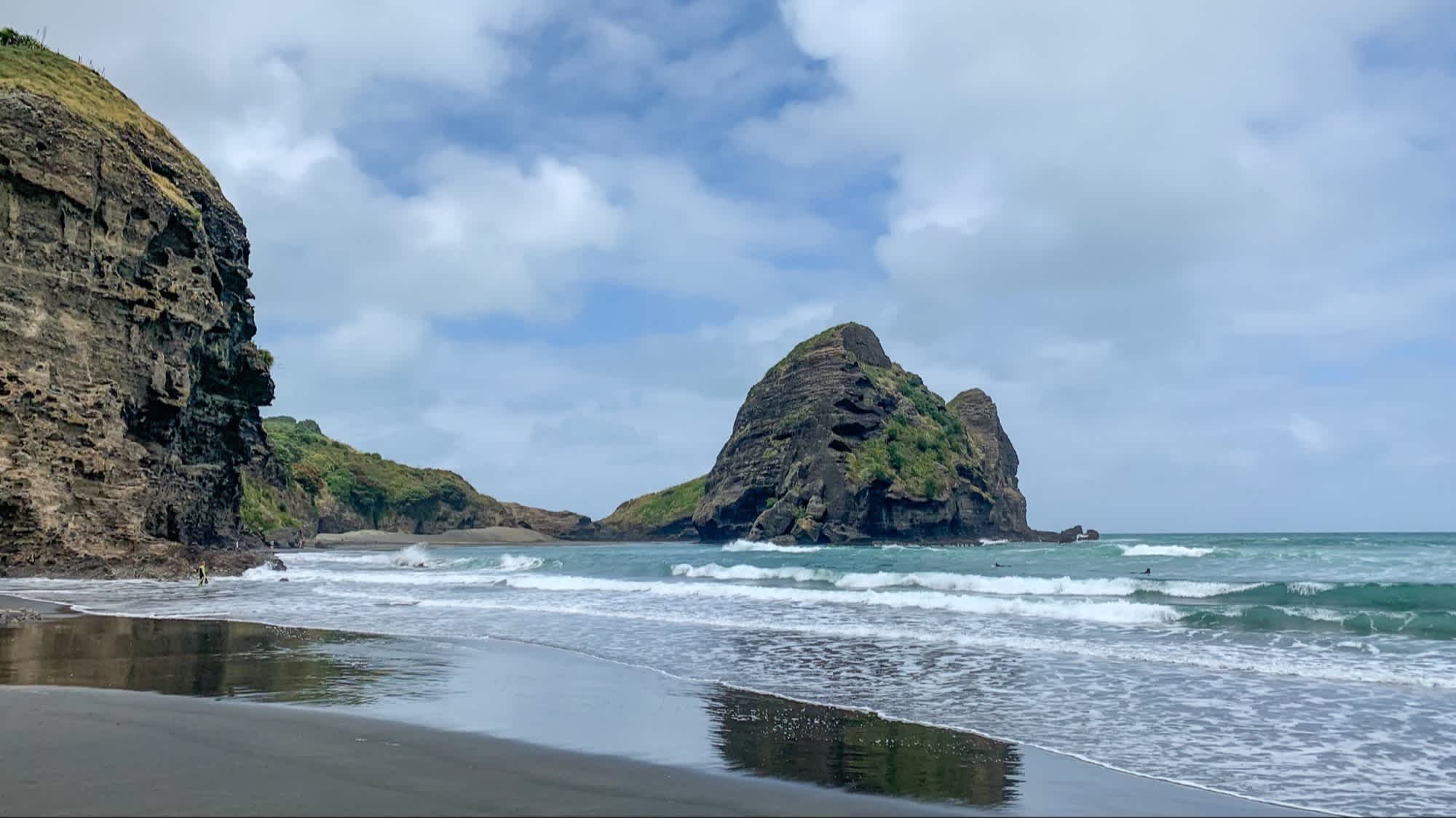 Der Strand Piha Beach in Auckland, Neuseeland mit Blick auf das Wasser und Felsen bei wolkigem Wetter.